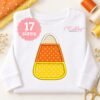Candy corn applique embroidered on a folded white shirt with coordinating orange and yellow sewing supplies.