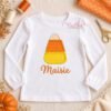 Candy corn applique on an open white shirt with Maisie embroidered below in orange thread.
