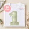 First birthday project mockup featuring a sage gingham number 1 applique with matching satin-stitch edging on a folded white shirt.