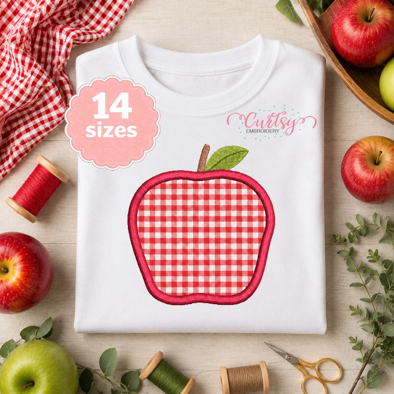 Apple applique embroidery design stitched on a folded white shirt with apples, thread and sewing supplies