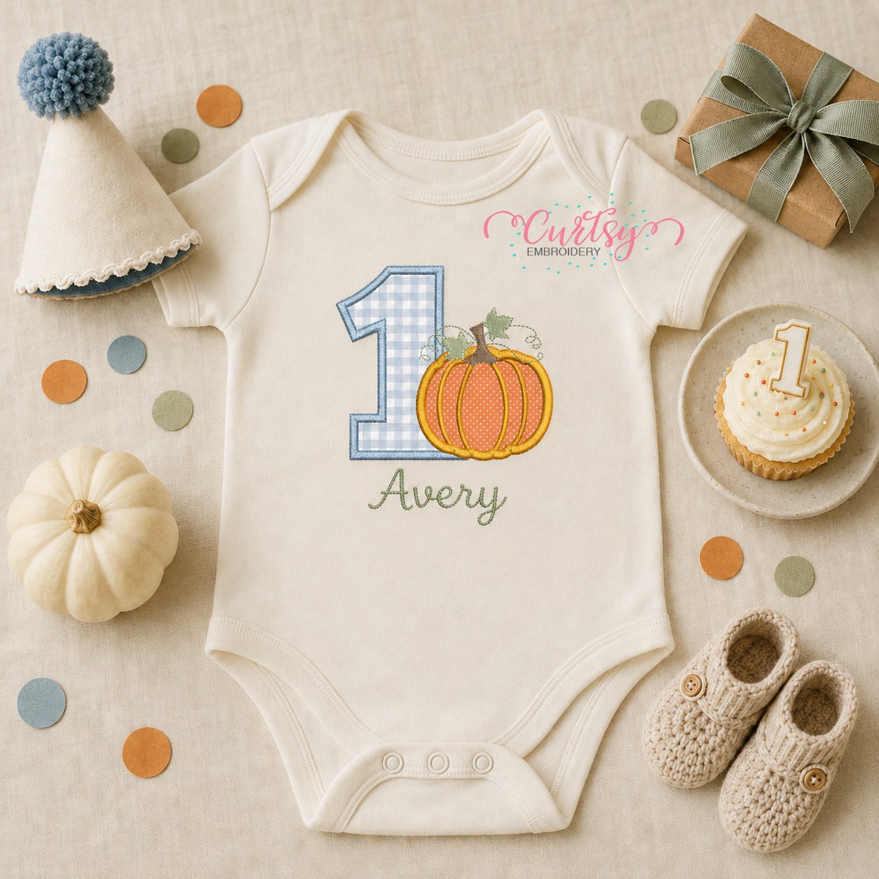 First birthday pumpkin applique embroidery design displayed on a folded white bodysuit