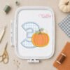 Number three pumpkin applique embroidery design displayed in a plastic machine embroidery hoop with fall sewing supplies.
