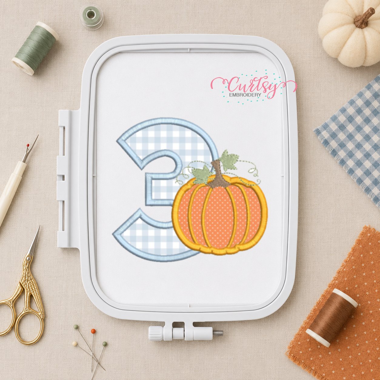 3rd Birthday Pumpkin Applique Design _ Logo 2 Number three pumpkin applique embroidery design displayed in a plastic machine embroidery hoop with fall sewing supplies.