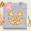 Jack O Lantern applique design displayed on a folded light gray shirt with matching embroidery props