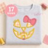 Girl jack o lantern applique embroidered on a folded gray sweatshirt with coordinating thread and fabric scraps