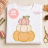 Stacked pumpkin applique on a folded white sweatshirt with orange gingham, cream Swiss dot and pink floral fabrics, a green leaf and light brown stem.