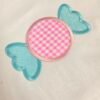 20261029_133330 Real stitched wrapped candy applique featuring a pink gingham fabric center, aqua wrapper sections, decorative stipple quilting, and satin stitch borders.