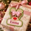Girl Reindeer Ornament Applique Design _ Logo 2 Girl reindeer applique ornament personalized with Emma, tied through its stitched eyelet to a pink ribbon on a wrapped present beneath a Christmas tree.