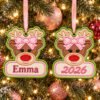 Girl Reindeer Ornament Applique Design _ Logo 3 Two girl reindeer applique ornaments with pink bows hanging on a Christmas tree, one personalized with Emma and the other embroidered with 2026.
