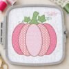 Pink motif pumpkin embroidery with patterned sections, a green stem, leaves, and curling vines on white fabric inside a gray plastic embroidery hoop.