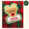 Untitled Tester stitch-out of the boy reindeer applique ornament with tan antlers, a red glitter nose, green border, and red 2026 lettering, photographed on red and green plaid fabric.